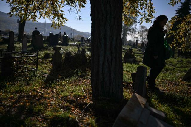 A Kosovo Serb woman visits the grave of her relative on All Souls' Day at the Orthodox cemetery in the ethnically divided Kosovo town of Mitrovica on November 1, 2025. Serbs from the north part of Mitrovica cross the river into the mainly Albanian Muslim south to pay respects to their lost ones during "Zadusnice," the Serbian Orthodox equivalent of "All Souls'Day", at the Orthodox graveyard, which was vandalized during the 1998-1999 war. (Photo by Armend NIMANI / AFP)