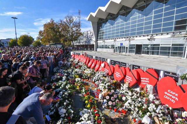 Mourners stand in front of flowers and heart-shaped signs bearing the names of victims layed outside the station during gathering marking the first anniversary of the Novi Sad railway station tragedy, in Novi Sad, on November 1, 2025. Tens of thousands gather in Serbia's second largest city Novi Sad to commemorate victims of a railway station collapse a year ago that triggered mass protests. On November 1, 2024, the collapse of the canopy at the newly-renovated railway station in Novi Sad killed 16 people. Regular student-led protests have gripped the Balkan nation since the tragedy, which became a symbol of entrenched corruption. (Photo by Nenad MIHAJLOVIC / AFP)