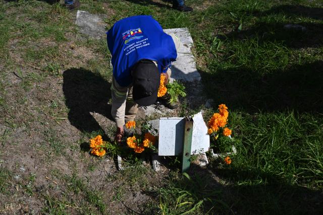 A municipal worker places flowers in memory of people buried as unknown in a mass grave at the Dolores Cemetery in Mexico City, on November 1, 2025, during an event organized by the National Search Commission (CNB), El Caracol A.C., and other civil society groups. (Photo by Yuri CORTEZ / AFP)