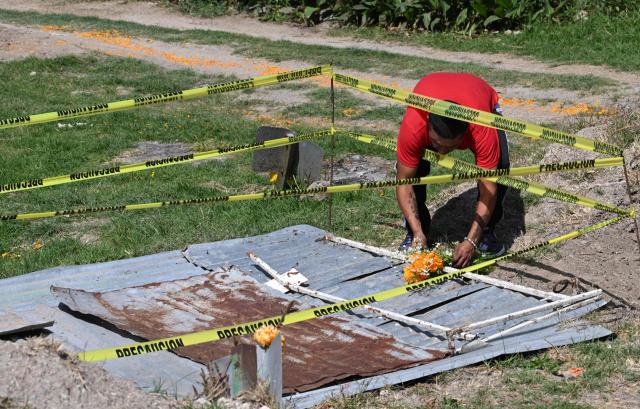 A man places flowers in memory of people buried as unknown in a mass grave at the Dolores Cemetery in Mexico City, on November 1, 2025, during an event organized by the National Search Commission (CNB), El Caracol A.C., and other civil society groups. (Photo by Yuri CORTEZ / AFP)