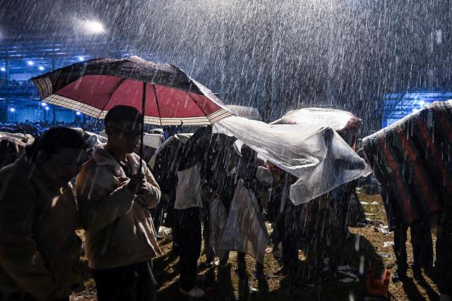 This photo taken on November 1, 2025 shows participants using an umbrella and plastic sheets to shield themselves from heavy rain during the Tazaungdaing Lighting Festival in Taunggyi, Myanmar’s northeastern Shan State. (Photo by Sai Aung MAIN / AFP)
