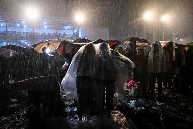 This photo taken on November 1, 2025 shows participants using plastic sheets and umbrellas to shield themselves from heavy rain during the Tazaungdaing Lighting Festival in Taunggyi, Myanmar’s northeastern Shan State. (Photo by Sai Aung MAIN / AFP)