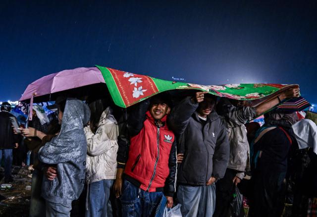 This photo taken on November 1, 2025 shows participants using a blankets and umbrellas to shield themselves from heavy rain during the Tazaungdaing Lighting Festival in Taunggyi, Myanmar’s northeastern Shan State. (Photo by Sai Aung MAIN / AFP)