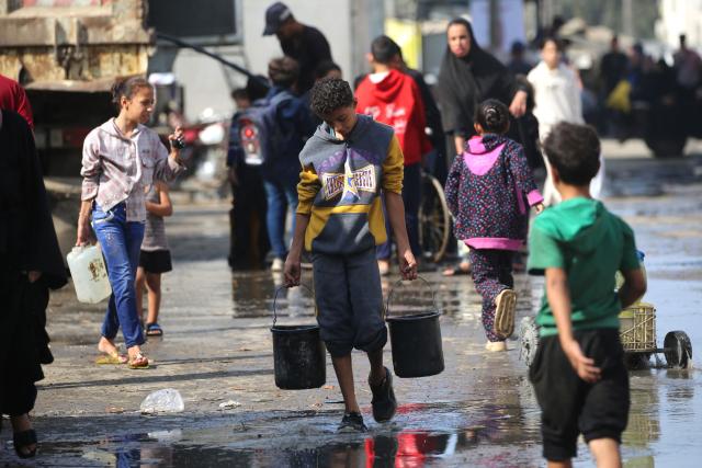 A Palestinian youth carries buckets of water, filled at a water collection point in a camp for displaced people in the Nuseirat refugee camp, located in the central Gaza Strip, on November 2, 2025. (Photo by EYAD BABA / AFP)