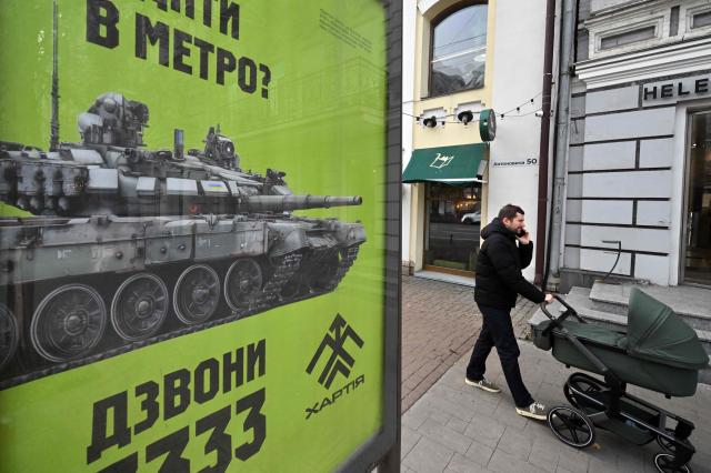 A man pushes a stroller past a recruiting placard of Ukraine's 13th Brigade of the National Guard Khartiya, depicting a tank and an announce reading "If you are tired of riding the subway, call us on 3333", in Kyiv on November 2, 2025, amid the Russian invasion of Ukraine. (Photo by Sergei SUPINSKY / AFP)