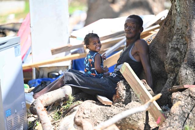 Clive Tomlinson, 55, sits under a tree with his two-year-old daughter Sarah amid rubble in Westmoreland, Jamaica, following the passage of Hurricane Melissa, on November 2, 2025. Planes and helicopters carrying humanitarian aid headed to Jamaica on October 31, three days after Melissa slammed into the island nation and killed at least 19 people.
Information Minister Dana Morris Dixon told a briefing that authorities had "quite credible" reports of possibly five additional deaths but had not yet been able to confirm. (Photo by Ricardo Makyn / AFP)