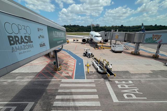 An aircraft stands on the tarmac at International Airport/Val-de-Cans–Julio Cezar Ribeiro with boarding gates decorated with references to COP30 in Belem, Para State, Brazil, on November 3, 2025. (Photo by Pablo PORCIUNCULA / AFP)