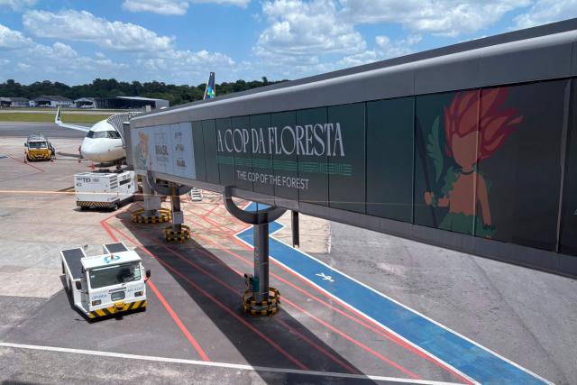 An aircraft stands on the tarmac at International Airport/Val-de-Cans–Julio Cezar Ribeiro with boarding gates decorated with references to COP30 in Belem, Para State, Brazil, on November 3, 2025. (Photo by Pablo PORCIUNCULA / AFP)
