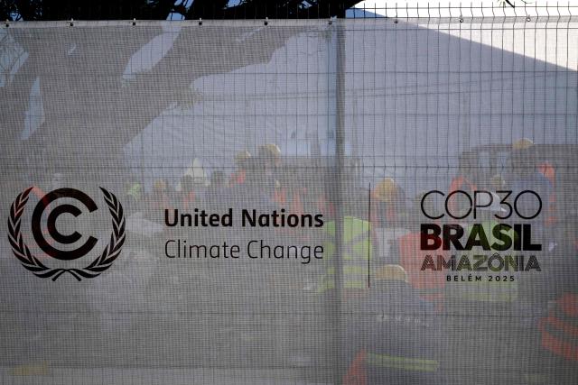 Workers rest behind a fence bearing the COP30 logo at a construction site in the City Park of the COP30, the United Nations Climate Change Conference in Belem, Para State, Brazil, taken on November 3, 2025. COP30, the United Nations Climate Change Conference, will be held on November 6 and 7. (Photo by Pablo PORCIUNCULA / AFP)