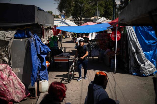 People walk past food stalls outside the Azteca Stadium in Mexico City on October 28, 2025. While millions celebrate Mexico hosting the FIFA World Cup for a third time, entire families of street vendors watch with concern as the football festivities threaten their long-standing source of income. (Photo by CARL DE SOUZA / AFP)