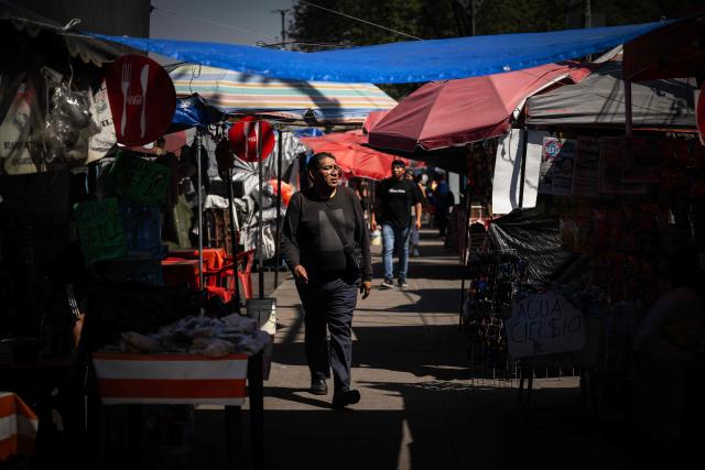 People walk past food stalls outside the Azteca Stadium in Mexico City on October 28, 2025. While millions celebrate Mexico hosting the FIFA World Cup for a third time, entire families of street vendors watch with concern as the football festivities threaten their long-standing source of income. (Photo by CARL DE SOUZA / AFP)