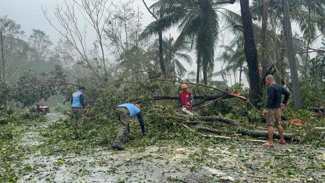 Policemen and residents clear a road of trees uprooted during Typhoon Kalmaegi in Silago, Leyte province on November 4, 2025. Residents sought refuge on rooftops and cars floated through flooded streets on November 4 as Typhoon Kalmaegi battered the central Philippines, leaving at least two people dead. (Photo by AFP)