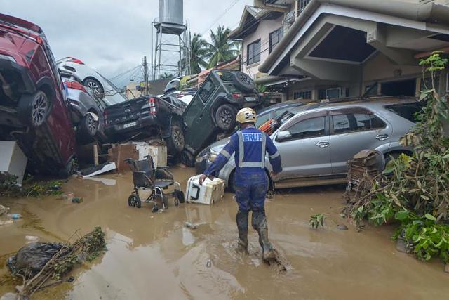 TOPSHOT - A rescuer walks past piled up cars washed away by floods at the height of Typhoon Kalmaegi in a subdivision of Cebu City in the central Philippines on November 4, 2025. Residents sought refuge on rooftops and cars floated through flooded streets on November 4 as Typhoon Kalmaegi battered the central Philippines, leaving at least two people dead. (Photo by Alan TANGCAWAN / AFP)