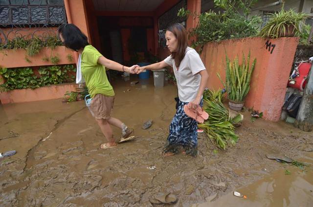 Residents walk along a muddy street following floods from heavy rains brought by Typhoon Kalmaegi in a subdivision of Cebu City in the central Philippines on November 4, 2025. Residents sought refuge on rooftops and cars floated through flooded streets on November 4 as Typhoon Kalmaegi battered the central Philippines, leaving at least two people dead. (Photo by Alan TANGCAWAN / AFP)