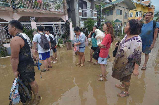 Residents stand in the mud as they wait to be evacuated from their flood-hit homes after Typhoon Kalmaegi hit the area in a subdivision of Cebu City in the central Philippines on November 4, 2025. Residents sought refuge on rooftops and cars floated through flooded streets on November 4 as Typhoon Kalmaegi battered the central Philippines, leaving at least two people dead. (Photo by Alan TANGCAWAN / AFP)