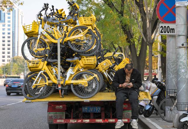 A man rests on a truck loaded with shared bicycles in Beijing on November 4, 2025. (Photo by Adek BERRY / AFP)
