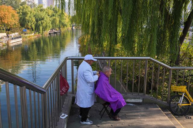 A man gets a haircut by a street barber on the banks of a water channel in Beijing on November 4, 2025. (Photo by Adek BERRY / AFP)