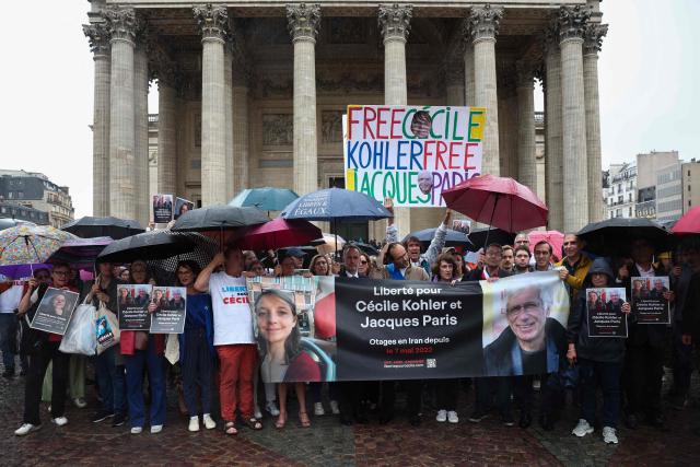 (FILES) Relatives and supporters pose behind a banner with the portrait of Cecile Kohler (L) and Jacaues Paris (R) who are being held in Iran since May 2022 on espionage charges, at the end of a rally in support to them at Place du Pantheon in Paris, on July 6, 2025. French teacher and trade unionist Cecile Kohler and former mathematics teacher Jacques Paris, who were arrested in May 2022 while on a tourist trip to Iran, were released after three years of captivity, said France's President Emmanuel Macron on November 4, 2025. (Photo by Sebastien DUPUY / AFP)