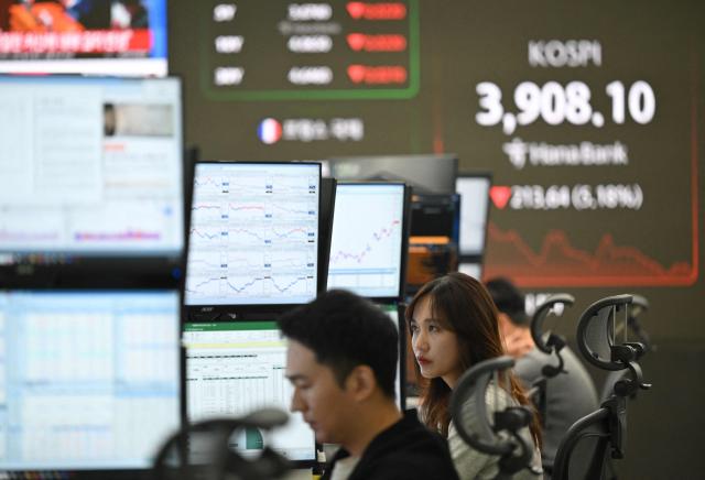 Currency dealers monitor exchange rates as a screen (R) shows South Korea's benchmark stock index in a foreign exchange dealing room at the Hana Bank headquarters in Seoul on November 5, 2025. Shares dropped in South Korea and Japan on November 5, on fears of overheated artificial intelligence valuations, with chip giants Samsung and SK hynix each losing over five percent. (Photo by Jung Yeon-je / AFP)