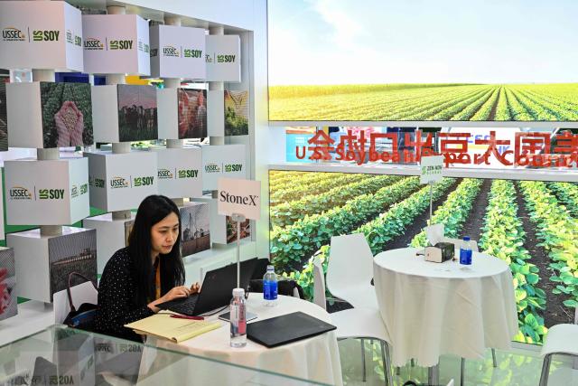 A woman is seen at a US Soybean Export Council stand during the 8th China International Import Expo (CIIE) in Shanghai on November 5, 2025. China said on November 5, it would extend a suspension of additional tariffs on US goods for one year, making official an agreement reached in talks between presidents Xi Jinping and Donald Trump last week. (Photo by Hector RETAMAL / AFP)