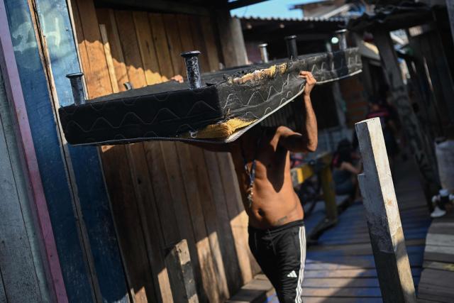 A man carries a mattress at Vila da Barca, a neighborhood of stilt houses in Belem, Para State, Brazil on November 5, 2025. (Photo by Mauro PIMENTEL / AFP)