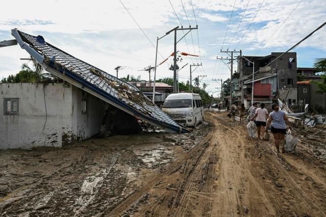 Residents walk along a mud covered street in the aftermath of Typhoon Kalmaegi in Liloan, in the province of Cebu on November 6, 2025. The death toll from Typhoon Kalmaegi in the central Philippines climbed past 100, as the devastating impact on Cebu province became clearer after the worst flooding in recent memory. (Photo by Jam STA ROSA / AFP)