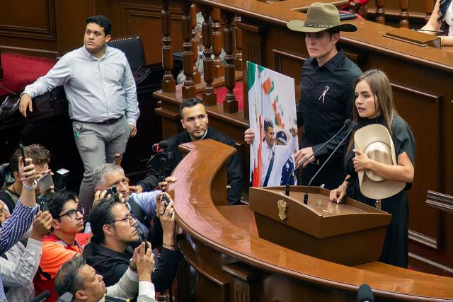 The widow of the late Mayor Carlos Manzo, Grecia Quiroz, accompanied by state representative Carlos Tafolla, delivers a speech at the Michoacan State Congress after being sworn in as Mayor of Uruapan in Uruapan, Michoacan State, Mexico on November 5, 2025. The Mexican government reported on November 2 that the mayor of Uruapan, Carlos Manzo, who was killed the previous night during a public event in the western state of Michoacan, had been under official protection since December last year. (Photo by Enrique Castro / AFP)