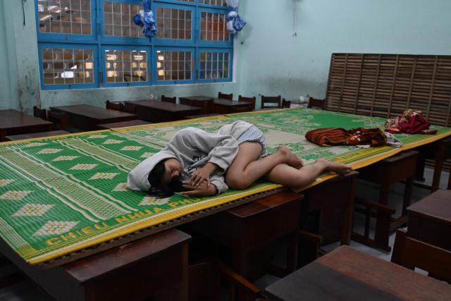TOPSHOT - A teenager uses her mobile phone as she lies on a mat placed on desks of a primary school, used to house people seeking temporary shelter from the incoming typhoon Kalmaegi, in Gia Lai province, central Vietnam on November 6, 2025. The typhoon is forecast to make landfall in central Vietnam late on November 6, bringing waves as high as eight metres (26 feet) and powerful storm surges, according to the national weather bureau. (Photo by NHAC NGUYEN / AFP)