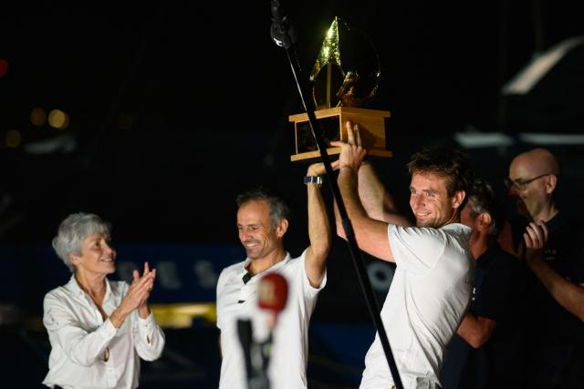 "SVR-LAZARTIGUE" ULTIM class multihull French skippers Franck Cammas (C) and Tom Laperche (R), receive the trophy by French astronaute and former minister Claudie Haignere (L) after winning the 17th edition of the Transat Cafe L'Or, off the shores of Fort-de-France, in the French overseas island of Martinique on November 5, 2025. Four open classes will take part in the race: IMOCA, Ocean Fifty, ULTIM and Class40. The Transat Cafe L'Or is a duo sailing race from Le Havre to Fort-de-France, in the French Caribbean island of Martinique. (Photo by Loic VENANCE / AFP)