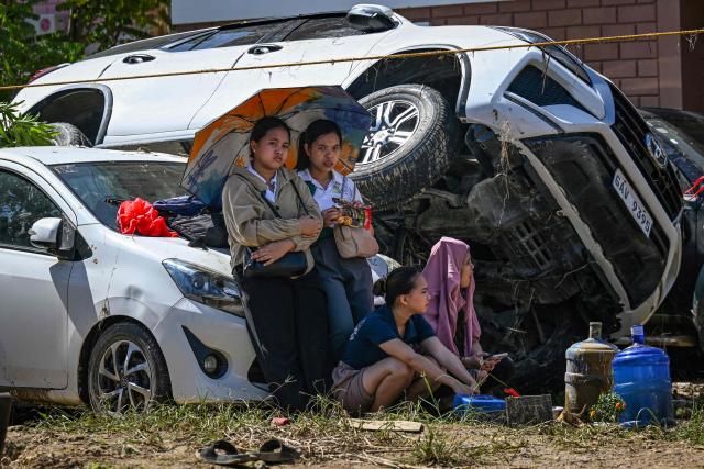 People rest beside cars, swept one on top of another by floodwaters caused by typhoon Kalmaegi, in Liloan in the province of Cebu on November 6, 2025. Typhoon Kalmaegi killed at least 140 people and left another 127 missing after unleashing devastating flooding across the central Philippines, official figures showed, as the storm headed towards Vietnam. (Photo by Jam STA ROSA / AFP)