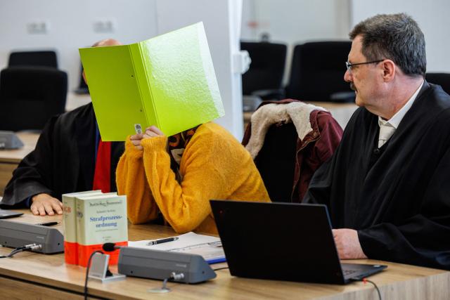 Defendant Susann E. hides behind a folder as she sits between her lawyers Uwe Schadt (L, hidden) and Hendrik Koenig in the courtroom at the start of her trial as suspected supporter of the far-right extremist cell National Socialist Underground (NSU), on November 6, 2025 at the Higher Regional Court of Dresden. The National Socialist Underground (NSU) was a neo-Nazi cell behind a string of racist murders of mostly Turkish and Greek-born immigrants across Germany between 2000 and 2007. (Photo by JENS SCHLUETER / POOL / AFP)