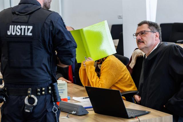 Defendant Susann E. hides behind a folder as she sits between her lawyers Uwe Schadt (L, hidden) and Hendrik Koenig in the courtroom at the start of her trial as suspected supporter of the far-right extremist cell National Socialist Underground (NSU), on November 6, 2025 at the Higher Regional Court of Dresden. The National Socialist Underground (NSU) was a neo-Nazi cell behind a string of racist murders of mostly Turkish and Greek-born immigrants across Germany between 2000 and 2007. (Photo by JENS SCHLUETER / POOL / AFP)