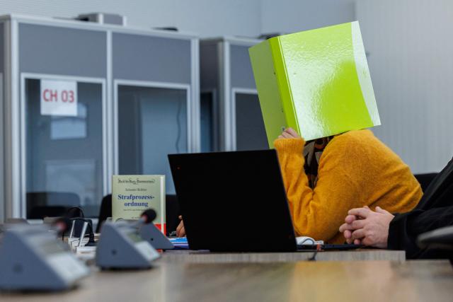 Defendant Susann E. hides behind a folder as she sits in the courtroom at the start of her trial as suspected supporter of the far-right extremist cell National Socialist Underground (NSU), on November 6, 2025 at the Higher Regional Court of Dresden. The National Socialist Underground (NSU) was a neo-Nazi cell behind a string of racist murders of mostly Turkish and Greek-born immigrants across Germany between 2000 and 2007. (Photo by JENS SCHLUETER / POOL / AFP)