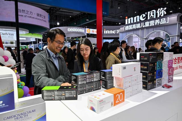 Visitors are seen at the General Nutrition Centers (GNC) stall during the 8th China International Import Expo (CIIE) in Shanghai on November 6, 2025. (Photo by Hector RETAMAL / AFP)