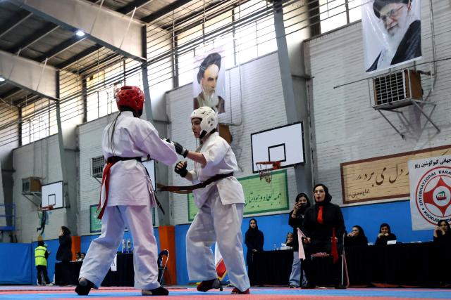 Images of Iran's late Supreme Leader Ruhollah Khomeini (L) and of Iran's second supreme leader Ali Khamenei, hang above the ring as two women fight during the women's karate competition, made-up of clubs and teams from around the Tehran province, in Tehran on November 6, 2025. Some 230 participants, including 5-year-old girls, took part in the competition, with team's deriving only from the Tehran province taking part. (Photo by ATTA KENARE / AFP)