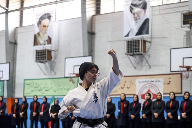 Images of Iran's late Supreme Leader Ruhollah Khomeini (L) and of Iran's second supreme leader Ali Khamenei, hang above the ring as an Iranian athlete warms up prior to the start of the women's karate competition, made-up of clubs and teams from around the Tehran province, in Tehran on November 6, 2025. Some 230 participants, including 5-year-old girls, took part in the competition, with team's deriving only from the Tehran province taking part. (Photo by ATTA KENARE / AFP)
