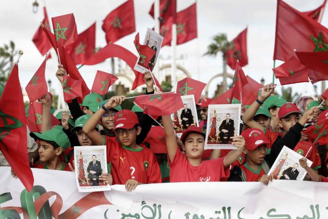Children wave Morocco's national flags and hold portraits of King Mohammed VI during commemorations of the so-called Green March of 1975, when 350,000 Moroccans marched to the border of what was then Spanish Sahara to pressure Madrid into handing over the territory, on Mechouar Square in Laayoune, the biggest city of the Western Sahara, on November 6, 2025. The UN Security Council voted on November 1, 2025 in favor of a resolution backing Morocco's autonomy plan for Western Sahara as the "most feasible" solution for the disputed territory, triggering celebrations in Rabat but angering Algeria. (Photo by Abdel Majid BZIOUAT / AFP)