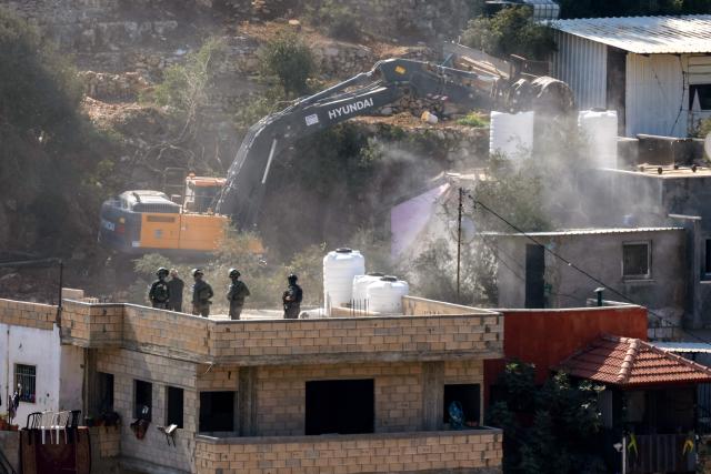 Isreali soldiers look on from the roof of a building as a military bulldozer demolishes a house belonging to a Palestinian family, in the occupied West Bank village of Qatanna, on November 6, 2025. (Photo by Zain JAAFAR / AFP)
