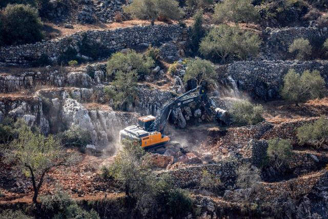 An Israeli military bulldozer uproots trees as it clears the way towards a house belonging to a Palestinian family that is scheduled to be demolished, in the occupied West Bank village of Qatanna, on November 6, 2025. (Photo by Zain JAAFAR / AFP)