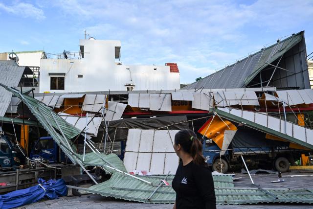 A woman looks at a damaged structure with a partially collpased roof in Quy Nhon in Gia Lai province, central Vietnam on November 7, 2025, after typhoon Kalmaegi hit the area. Typhoon Kalmaegi swept across Vietnam early on November 7, weakening into a tropical storm after claiming at least 188 lives in the Philippines. (Photo by Nhac NGUYEN / AFP)