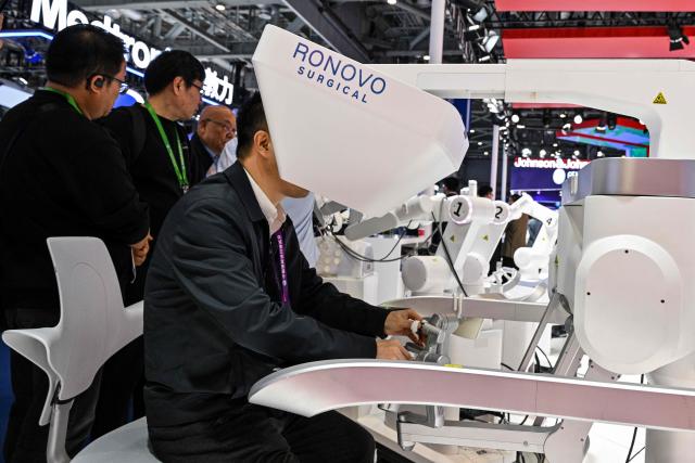 A visitor checks a robotic surgical equipment in the Ronovo stand during the 8th China International Import Expo (CIIE) in Shanghai on November 7, 2025. (Photo by Hector RETAMAL / AFP)