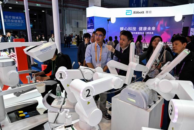 Visitors look at robotic surgical equipments in the Ronovo stand during the 8th China International Import Expo (CIIE) in Shanghai on November 7, 2025. (Photo by Hector RETAMAL / AFP)