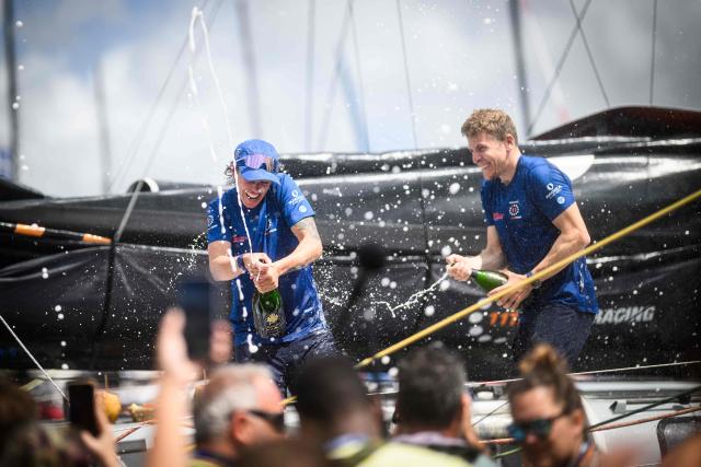 11th Hour Racing Imoca monohull skippers Italian Francesca Clapcich (L) and British Will Harris (R) spray champagne as they celebrate coming second in the Imoca class 17th edition of the Transat Cafe L'Or, off shores Fort-de-France, in the French overseas island of Martinique on November 7, 2025. Four open classes take part in the race: IMOCA, Ocean Fifty, ULTIM and Class40. The Transat Cafe L'Or is a duo sailing race from Le Havre to Fort-de-France, in the French Caribbean island of Martinique. (Photo by Loic VENANCE / AFP)
