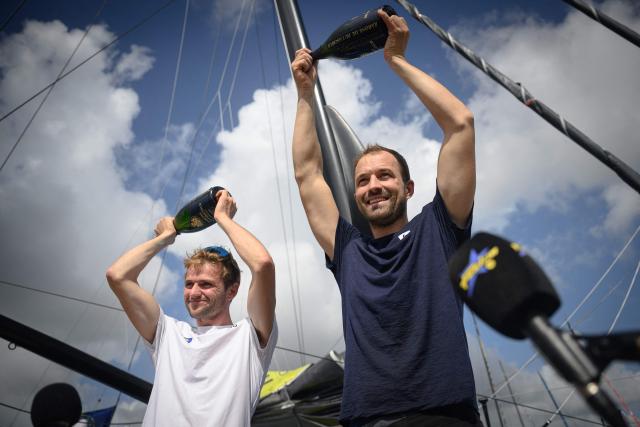 Macif Sante Prevoyance Imoca monohull skippers Sam Goodchild (C) and Lois Berrehar (L) lift bottles of champagne above their heads as they celebrate finishing third in the Imoca class 17th edition of the Transat Cafe L'Or, off the shores of Fort-de-France, in the French overseas island of Martinique, on November 7, 2025. Four open classes take part in the race: IMOCA, Ocean Fifty, ULTIM and Class40. The Transat Cafe L'Or is a duo sailing race from Le Havre to Fort-de-France, in the French Caribbean island of Martinique. (Photo by Loic VENANCE / AFP)