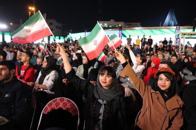 Iranian women wave national flags during the unveiling of a statue (unseen) depicting Sasanian king Shapur I capturing Roman emperor Valerian, at Enghelab (Revolution) Square in the capital Tehran on November 7, 2025. The event was the latest in a series of unveiling national symbols following Iran's recent 12-day war with Israel in June. The statue was modelled on an original stone engraving in southern Iran, symbolising Iranian triumph over foreign foes. (Photo by AFP)