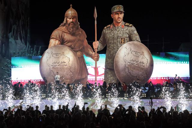 Iranians stand before a stage as an orchestra performs beneath a large banner during the unveiling of a statue (unseen) depicting Sasanian king Shapur I capturing Roman emperor Valerian, at Enghelab (Revolution) Square in the capital Tehran on November 7, 2025. (Photo by AFP)