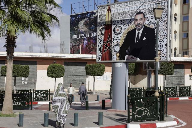 Pedestrians walk past a portrait of Morocco's King Mohammed VI in Laayoune, the main city of Moroccan-controlled Western Sahara, on November 7, 2025. The UN Security Council voted on October 31, 2025 in favor of a resolution backing Morocco's autonomy plan for Western Sahara as the "most feasible" solution for the disputed territory, triggering celebrations in Rabat but angering Algeria. (Photo by Abdel Majid BZIOUAT / AFP)