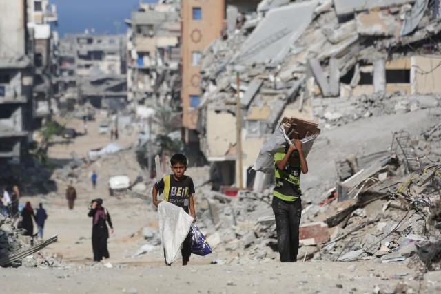 Palestinian boys carry pieces of wood as they make their way through the rubble of destroyed buildings in the Al-Shatee refugee camp, east of Gaza City, on November 8, 2025. Despite some progress in delivering food to Gazans, the territory, ravaged by war and wracked by hunger, remains in urgent need of humanitarian assistance, a UN spokesperson said on November 7. A ceasefire between Israel and Hamas came into effect on October 10, after both sides agreed to a US-brokered 20-point peace plan. (Photo by Bashar Taleb / AFP)
