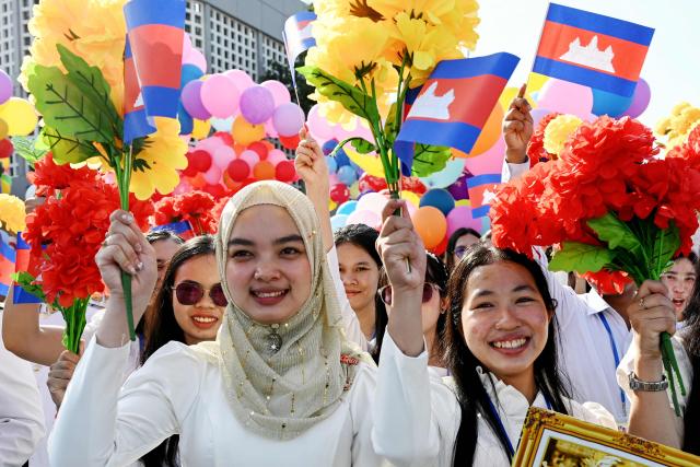 Women hold up flowers and national flags during a ceremony marking Cambodia's 72nd Independence Day celebrations at the Independence Monument in Phnom Penh on November 9, 2025. (Photo by TANG CHHIN Sothy / AFP)
