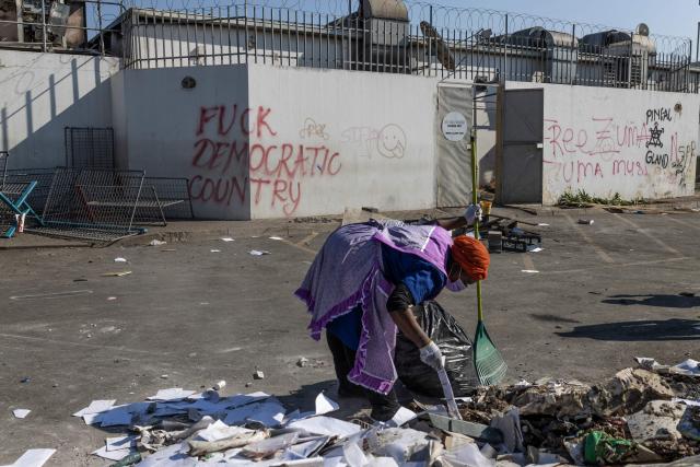 (FILES) A woman uses a rake to clean debris outside of the looted Dube Village Mall in Durban on July 17, 2021. After the area was severely affected for several days by looting and unrest, local residents are trying to return to normality. The trial of Duduzile Zuma-Sambudla, daughter of South Africa's former president Jacob Zuma, accused of inciting 2021 riots that left more than 350 people dead, was set by the Durban High Court to start November 10, 2025.
Duduzile Zuma-Sambudla, 42, is among several people charged with inciting terrorism and public violence via posts on social media after Zuma was sent to prison in July 2021 for refusing to testify in corruption proceedings against him.
The explosion of rioting and looting that followed was the deadliest unrest in South Africa since the fall of the white-minority government in 1994. 
Zuma-Sambudla denies the charges and claims the case is politically motivated. (Photo by GUILLEM SARTORIO / AFP)